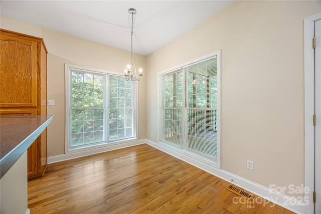 unfurnished dining area featuring a chandelier, baseboards, and light wood finished floors