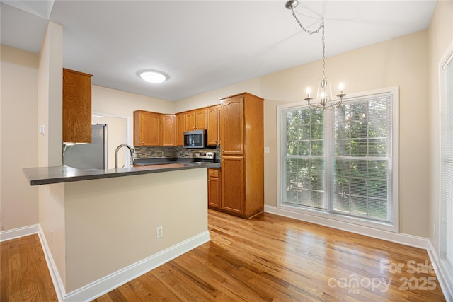 kitchen with stainless steel appliances, a peninsula, dark countertops, a chandelier, and a sink
