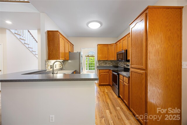 kitchen with appliances with stainless steel finishes, a peninsula, light wood-style floors, and decorative backsplash