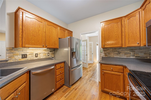 kitchen featuring stainless steel appliances, tasteful backsplash, light wood finished floors, brown cabinets, and dark countertops