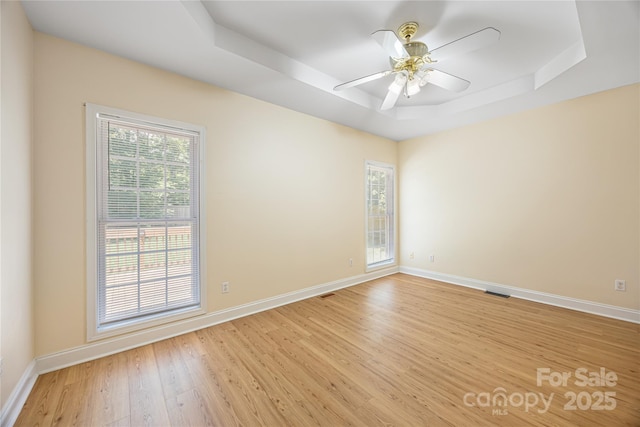 unfurnished room featuring a tray ceiling, light wood finished floors, plenty of natural light, and baseboards