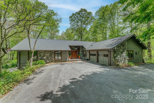 view of front of house featuring an attached garage, aphalt driveway, roof with shingles, and stone siding