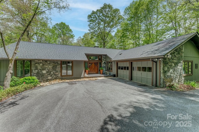 ranch-style home with roof with shingles, an attached garage, driveway, and stone siding