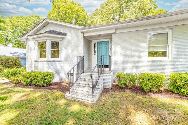 view of exterior entry featuring a lawn and brick siding