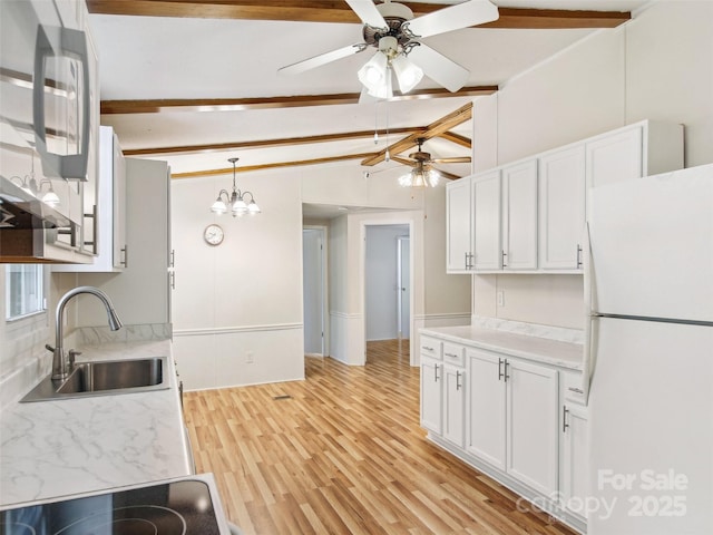 kitchen featuring ceiling fan, a sink, freestanding refrigerator, vaulted ceiling with beams, and white cabinetry