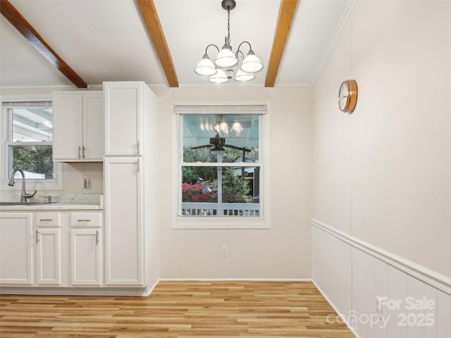 unfurnished dining area with a sink, beamed ceiling, light wood-type flooring, and a notable chandelier