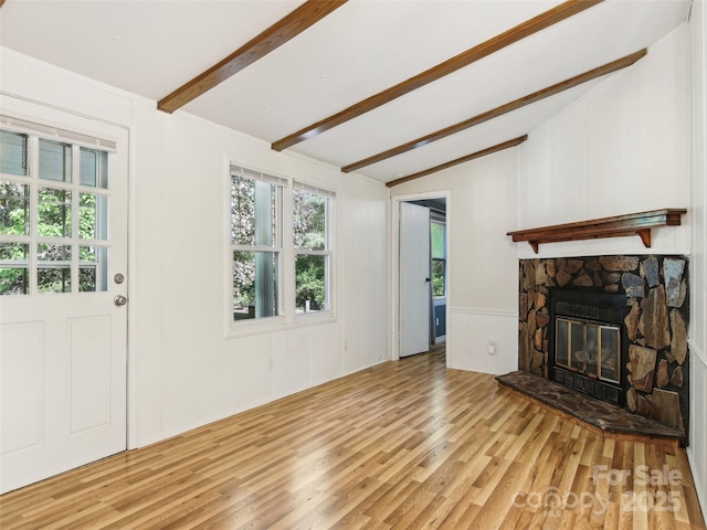 unfurnished living room featuring a decorative wall, lofted ceiling with beams, wood finished floors, and a fireplace