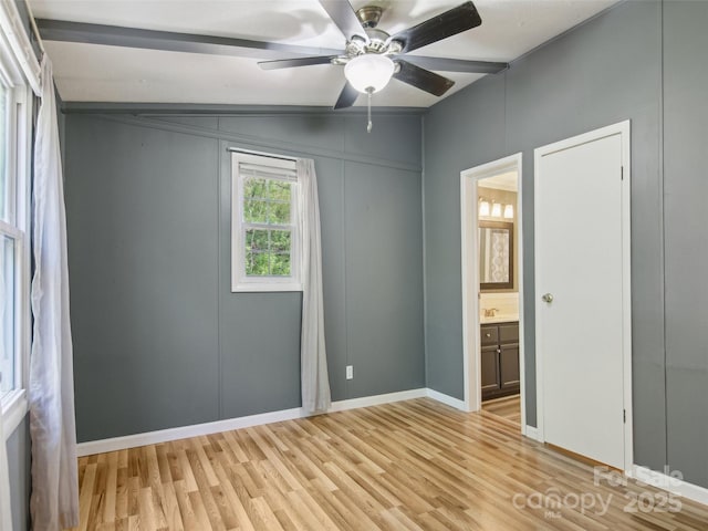 unfurnished bedroom featuring a decorative wall, light wood-style floors, baseboards, ceiling fan, and ensuite bath