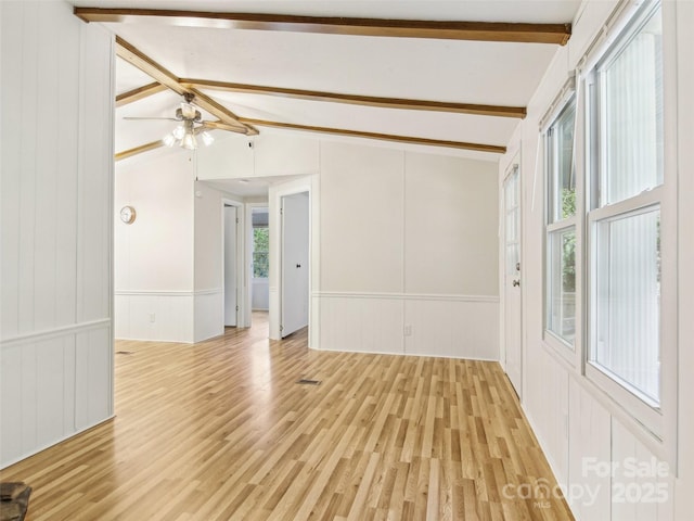 spare room with a wainscoted wall, ceiling fan, lofted ceiling with beams, and light wood-type flooring