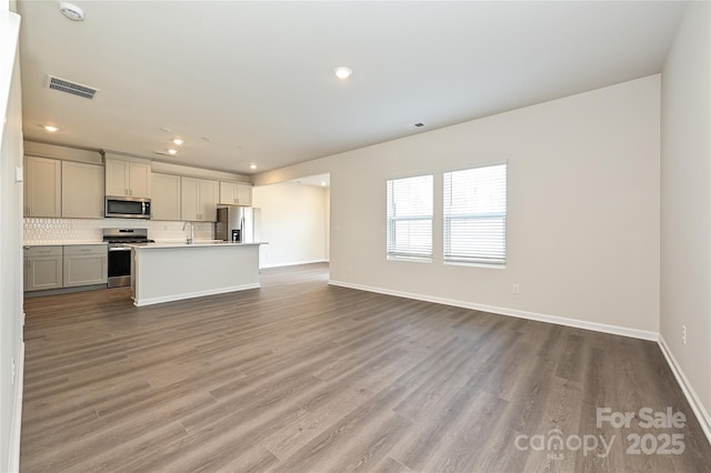 unfurnished living room with visible vents, wood finished floors, a sink, baseboards, and recessed lighting