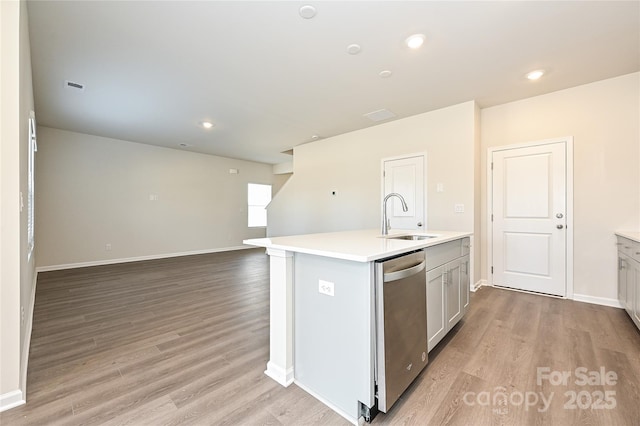 kitchen with a kitchen island with sink, stainless steel dishwasher, light wood-type flooring, a sink, and light countertops
