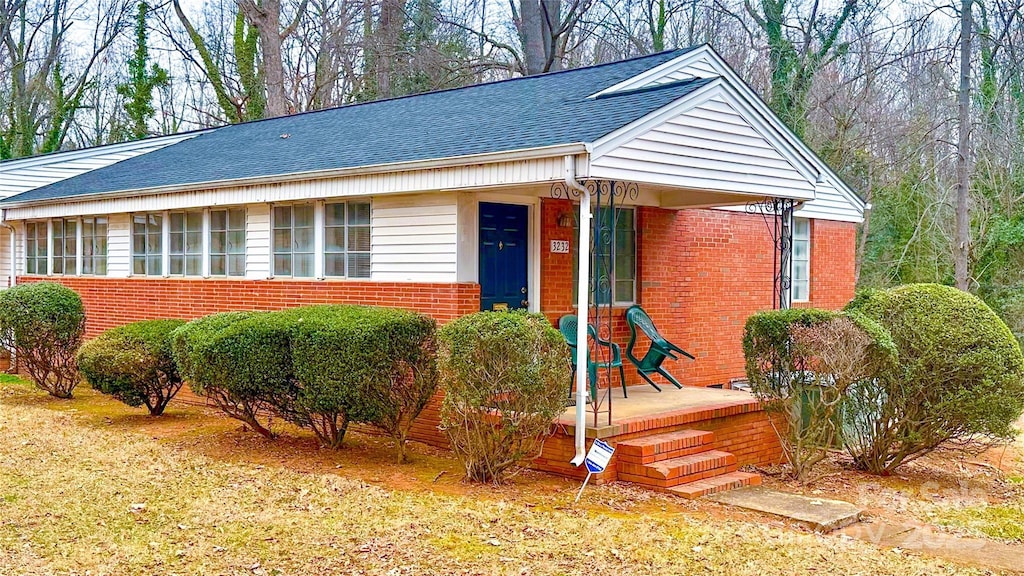 view of front of property featuring brick siding, roof with shingles, and a porch