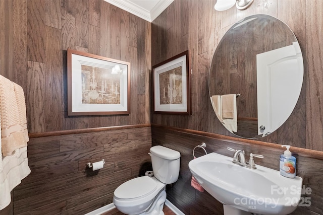 bathroom with a sink, toilet, crown molding, and wooden walls