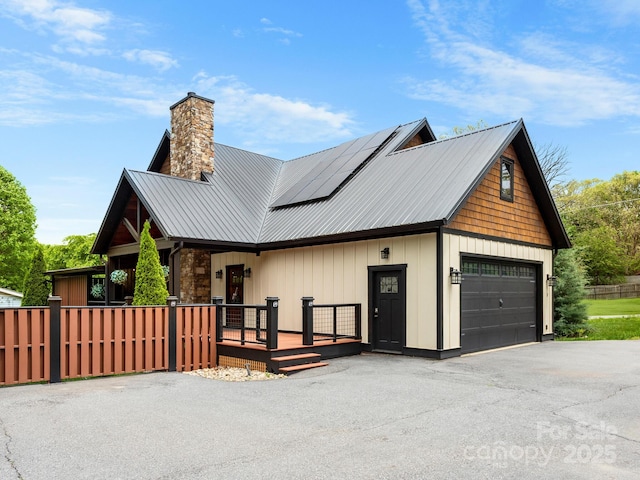 view of property exterior featuring covered porch, roof mounted solar panels, a chimney, metal roof, and asphalt driveway