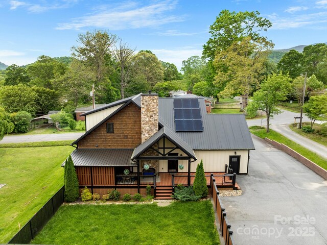 rear view of property featuring metal roof, a chimney, roof mounted solar panels, and a wooden deck