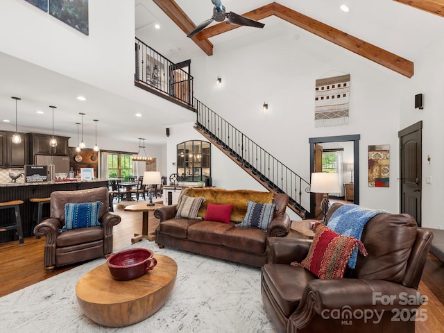 living room with high vaulted ceiling, ceiling fan, wood finished floors, beamed ceiling, and stairway