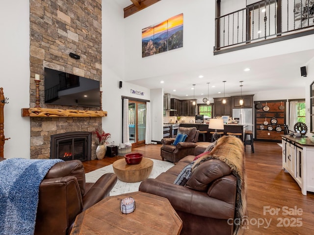 living room with wood finished floors, a high ceiling, a stone fireplace, and recessed lighting