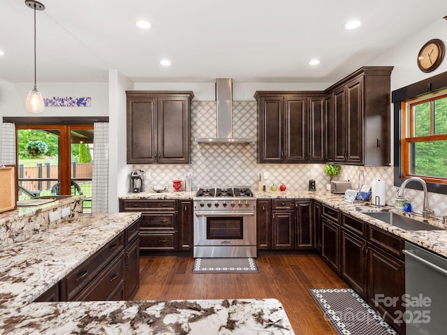 kitchen featuring stainless steel appliances, wall chimney range hood, a sink, light stone countertops, and recessed lighting