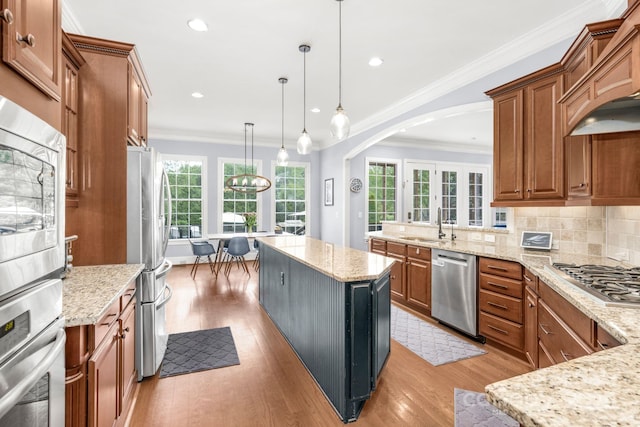kitchen with arched walkways, appliances with stainless steel finishes, brown cabinetry, and light wood-style floors