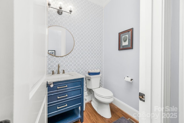 half bathroom featuring vanity, wood finished floors, toilet, baseboards, and wallpapered walls