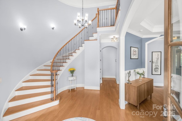 foyer entrance featuring arched walkways, ornamental molding, stairs, and wood finished floors