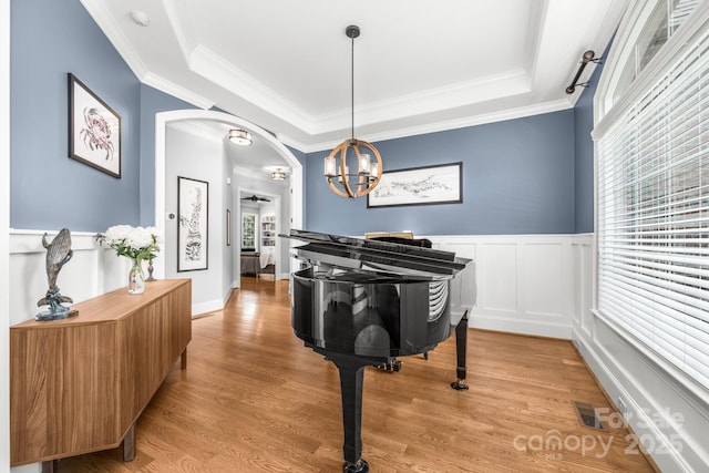 sitting room with an inviting chandelier, crown molding, visible vents, a raised ceiling, and arched walkways