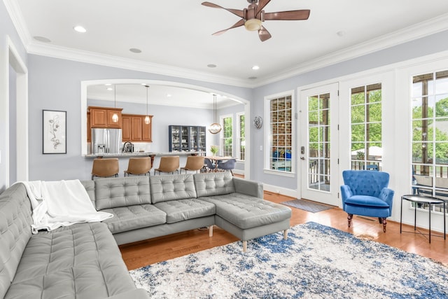 living area featuring crown molding, arched walkways, ceiling fan, and light wood finished floors