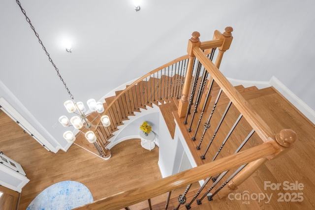 staircase featuring baseboards, an inviting chandelier, and wood finished floors