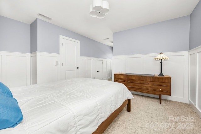 carpeted bedroom with visible vents, a decorative wall, and a wainscoted wall