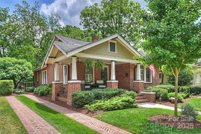 craftsman house with roof with shingles, a front lawn, brick siding, a porch, and a chimney