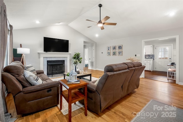 living area with a brick fireplace, lofted ceiling, baseboards, a ceiling fan, and light wood finished floors