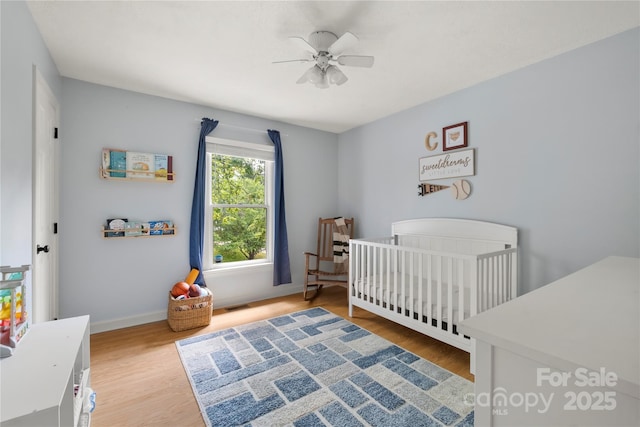 bedroom with a crib, a ceiling fan, baseboards, wood finished floors, and visible vents