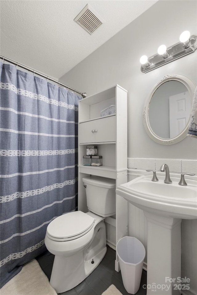 bathroom featuring visible vents, toilet, a textured ceiling, tile patterned floors, and a sink