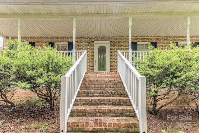 view of exterior entry featuring brick siding and covered porch