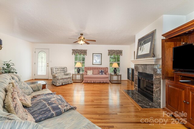 living area with a premium fireplace, ceiling fan, light wood-style flooring, and healthy amount of natural light