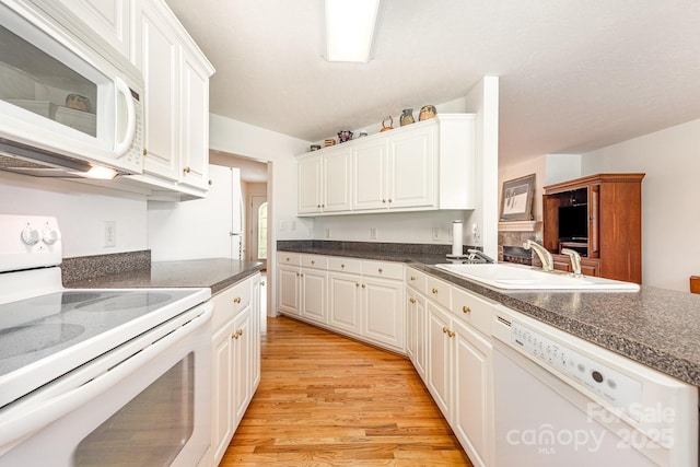 kitchen featuring white appliances, a sink, light wood finished floors, white cabinets, and dark countertops
