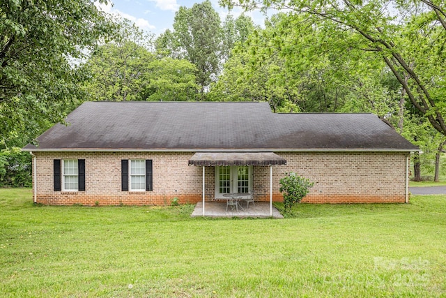 view of front facade with a front yard, brick siding, a patio area, and roof with shingles