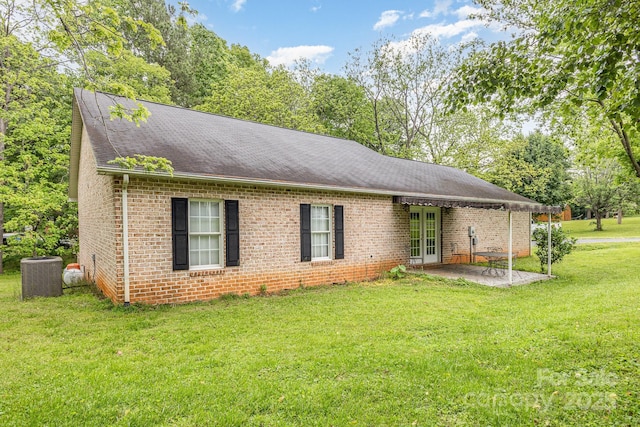 single story home featuring cooling unit, a patio area, brick siding, a front lawn, and roof with shingles
