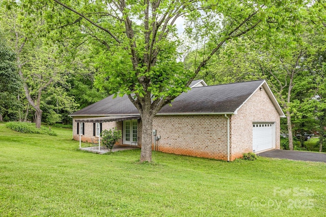 view of side of property featuring brick siding, a yard, asphalt driveway, and roof with shingles