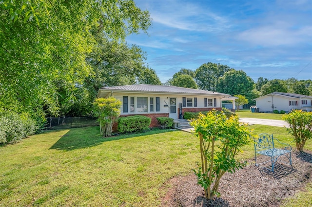 view of front of home with fence, a front lawn, brick siding, concrete driveway, and metal roof