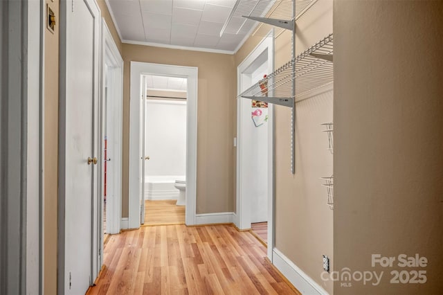 hallway featuring light wood-style floors, baseboards, and crown molding