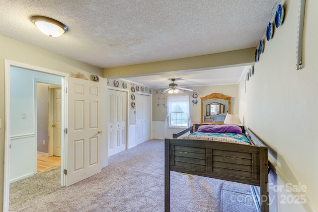carpeted bedroom featuring a textured ceiling, multiple closets, and baseboards
