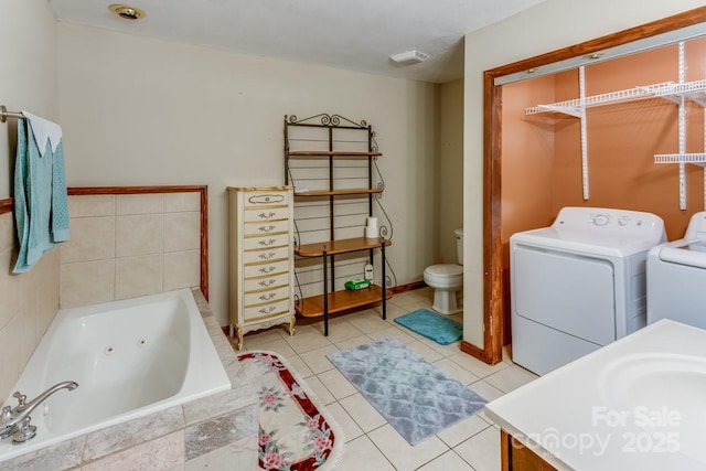 full bath with tile patterned flooring, a tub with jets, washing machine and dryer, and toilet