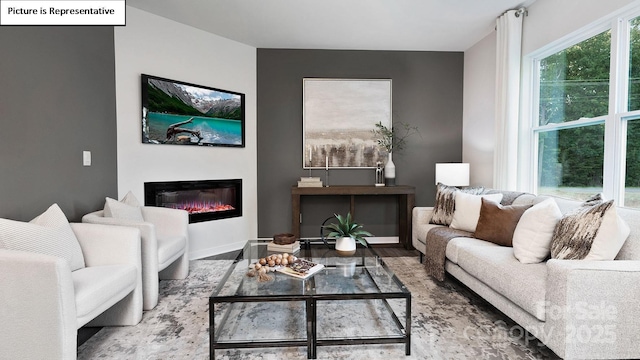 living area featuring a glass covered fireplace, baseboards, and wood finished floors