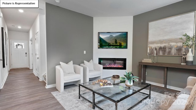 living room featuring a glass covered fireplace, baseboards, recessed lighting, and wood finished floors