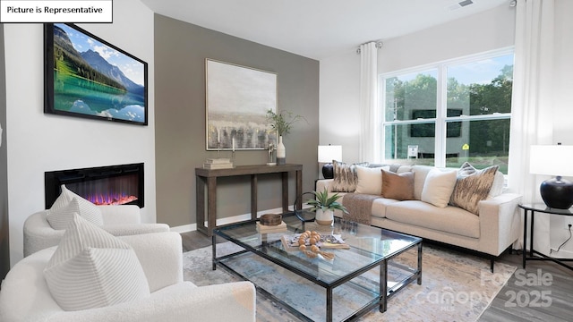 living area with a glass covered fireplace, baseboards, wood finished floors, and visible vents