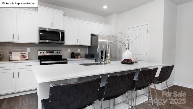 kitchen featuring white cabinets, appliances with stainless steel finishes, a sink, an island with sink, and tasteful backsplash