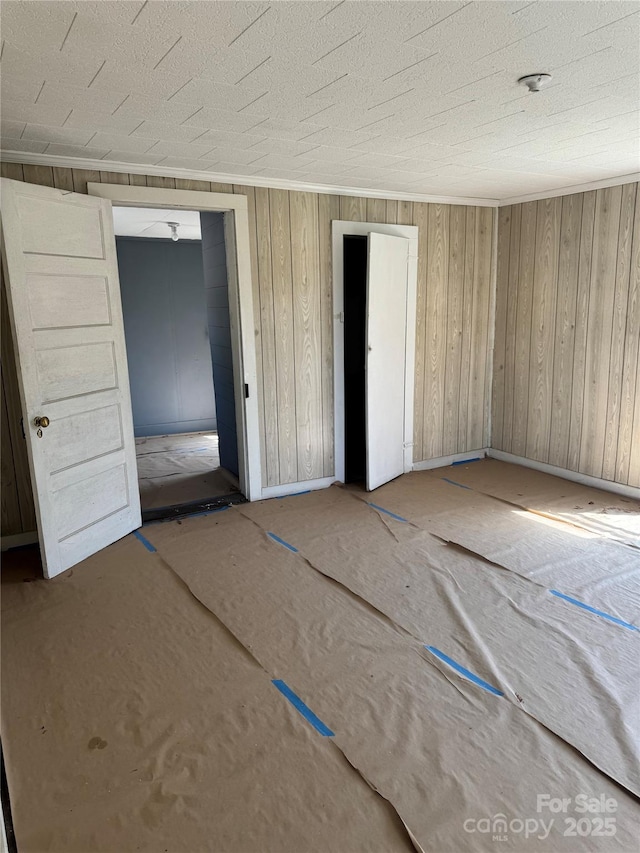 unfurnished bedroom featuring wooden walls, baseboards, and a textured ceiling