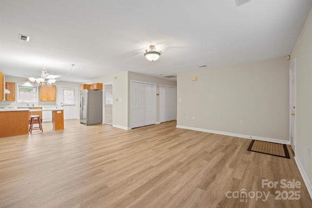 unfurnished living room with baseboards, visible vents, light wood-type flooring, and a chandelier