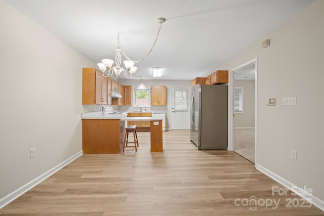 kitchen featuring freestanding refrigerator, a peninsula, a breakfast bar, a chandelier, and range